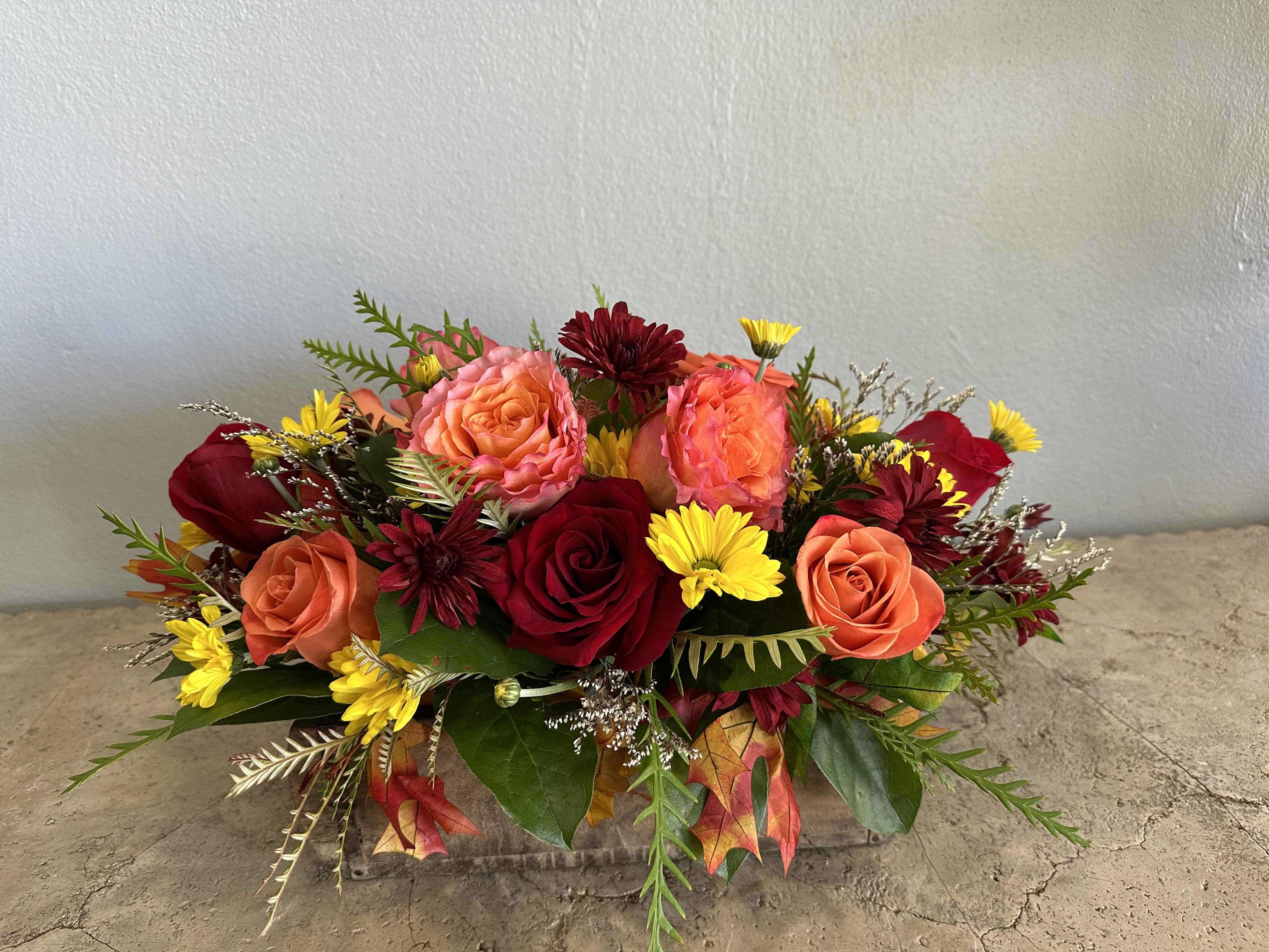 Arrangement of red and peach roses with yellow daisies in a low container