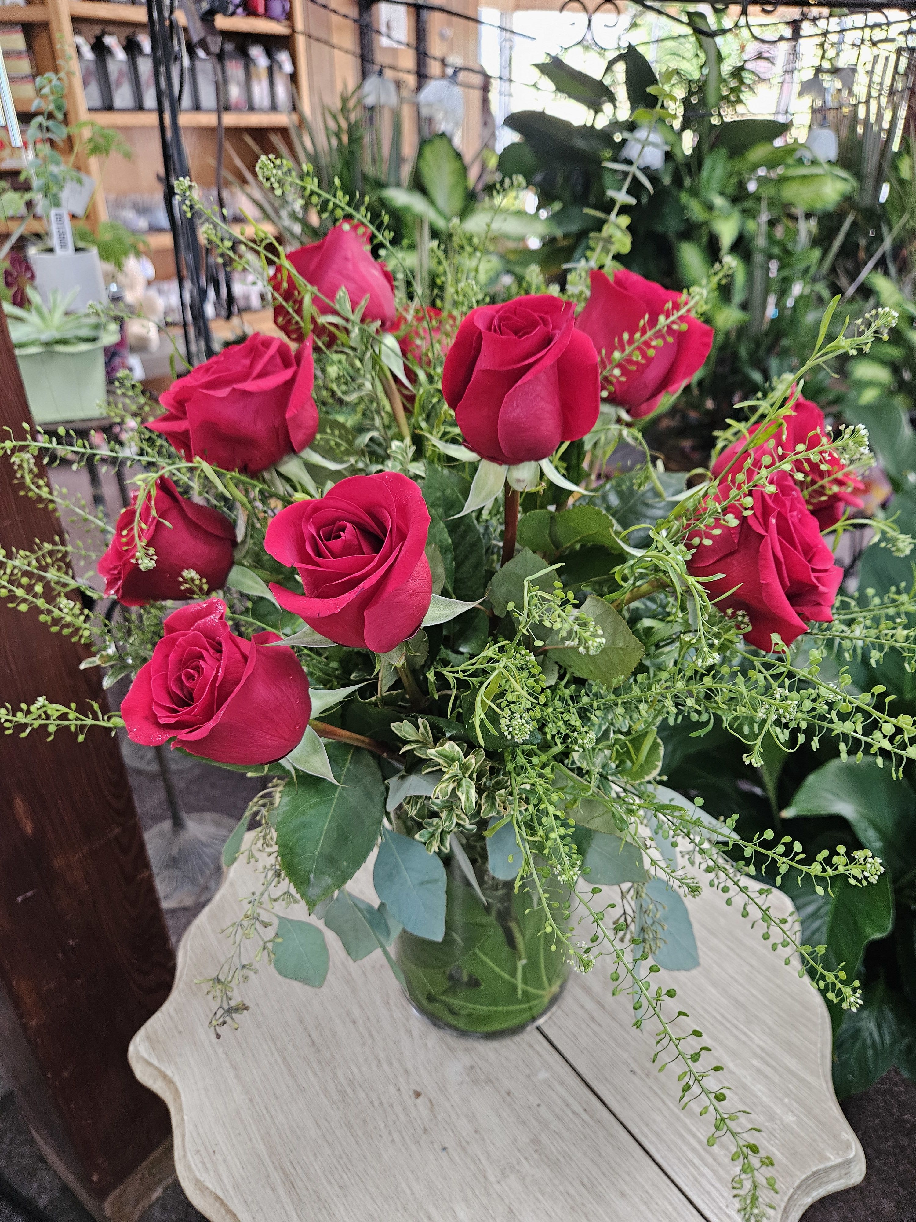Arrangement of red roses with filler in a clear glass vase on a light wooden table