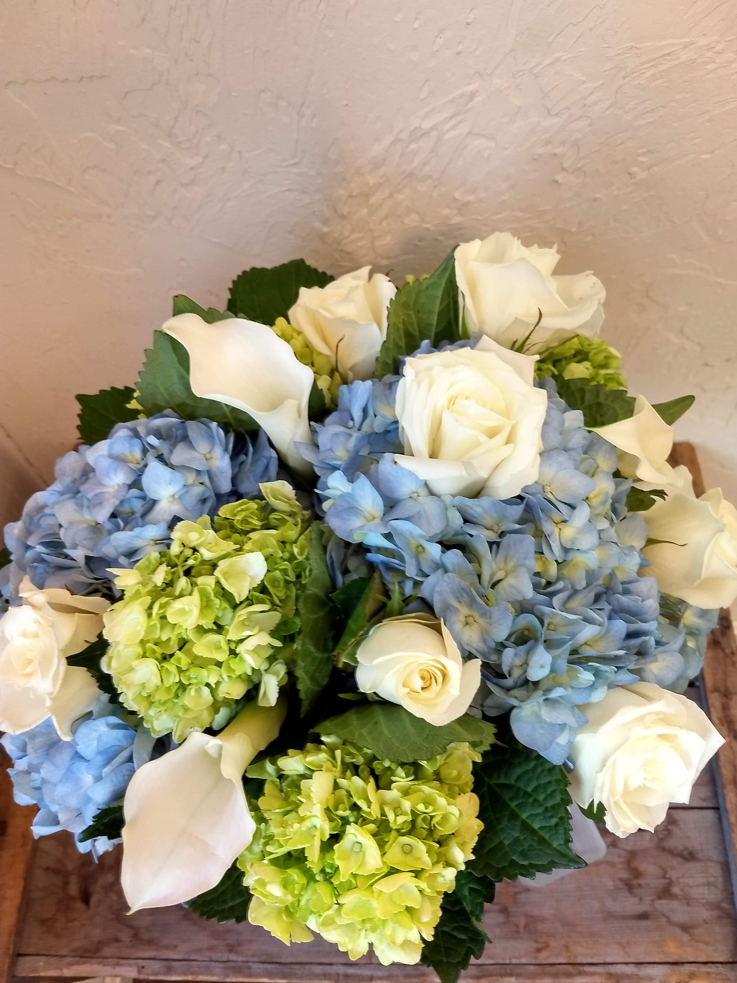 Clouds - Clouds Elegant and timeless, Clouds is a lovely floral arrangement that captures the soft beauty of a clear sky. This classic design features:  Pristine white roses  Graceful mini calla lilies  A base of soft light blue and green hydrangea  Accented with lush mixed greens Serene and sophisticated, this arrangement brings a sense of calm and refined beauty to any setting.
