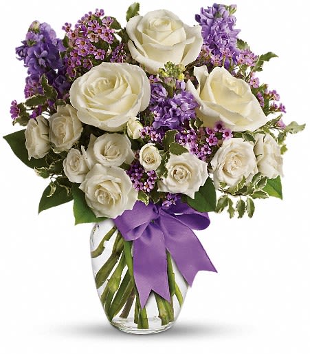 White roses and purple flowers arranged in a glass vase with a purple ribbon