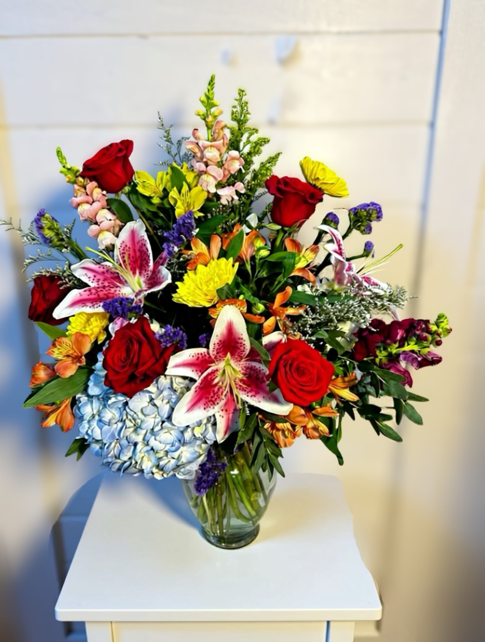 Mixed bouquet of red roses, lilies, and hydrangeas in a glass vase