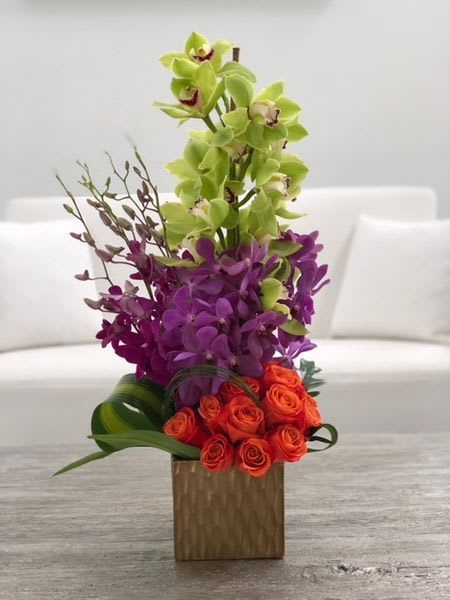 Tall orchid arrangement with orange roses in a wooden vase