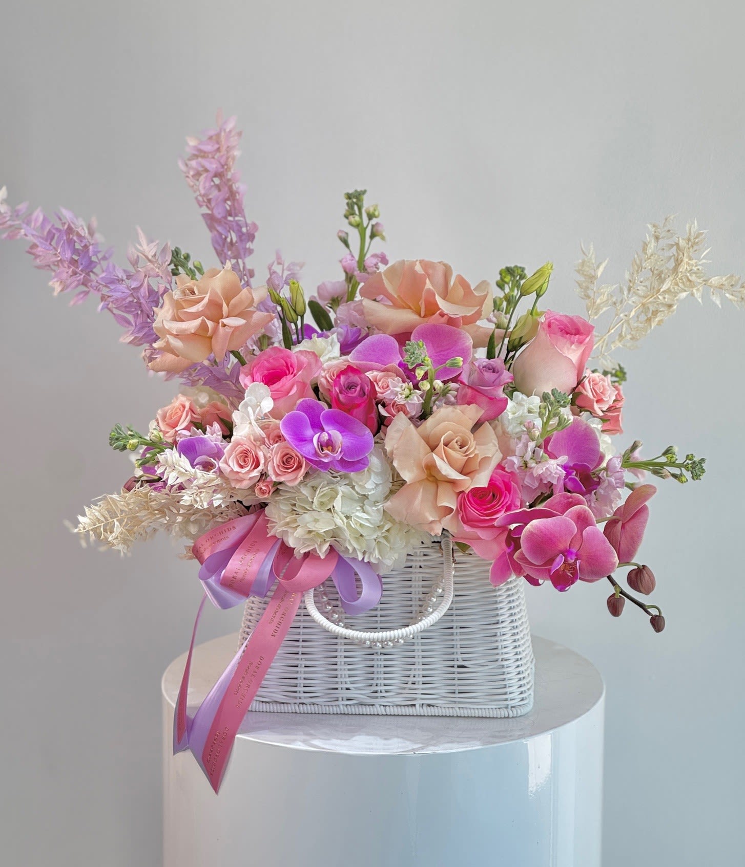 Pink and peach roses with orchids in a white wicker basket