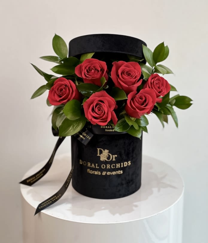 Amore - round box ™ - Elegant and timeless, this arrangement showcases velvety red roses surrounded by lush greenery. Set in a luxurious red velvet hatbox tied with satin ribbon, it radiates romance and sophistication.