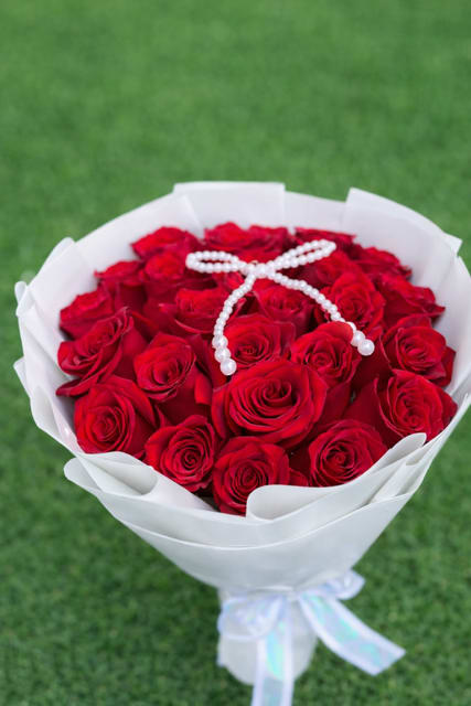 Bouquet of red roses wrapped in white paper with a pearl ribbon