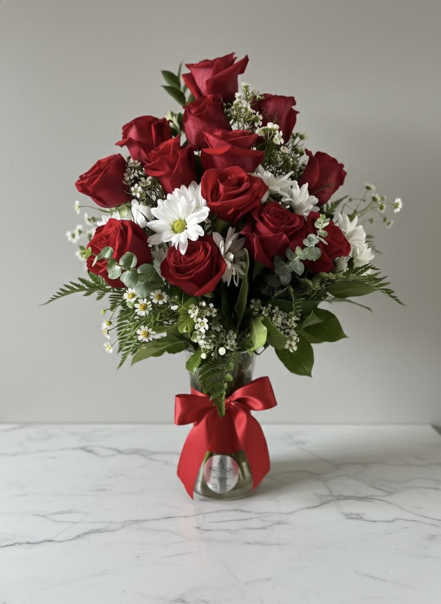 Red roses and white daisies arranged in a glass vase with a red ribbon.