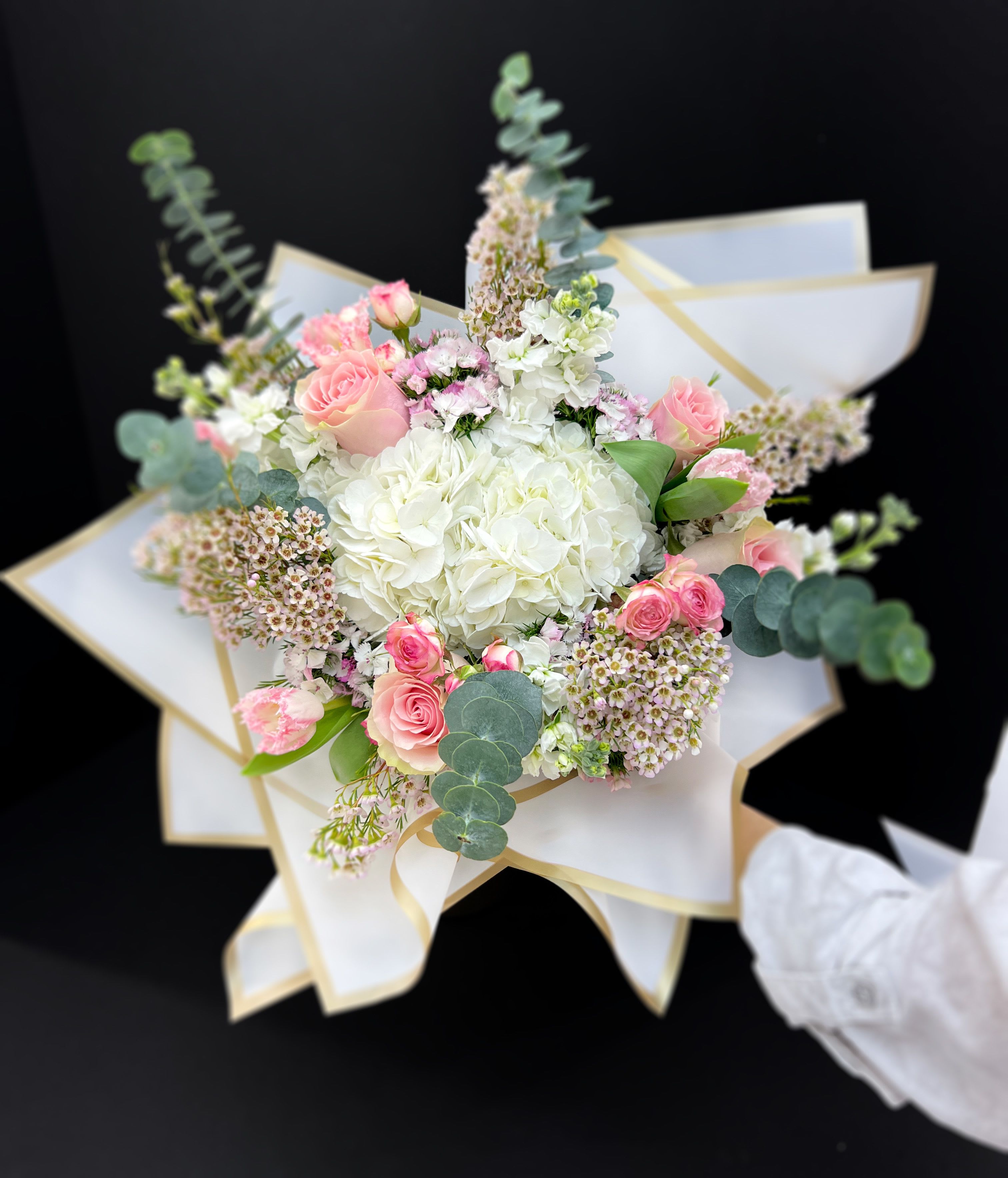 Bouquet of pink and white flowers wrapped in white paper with gold trim