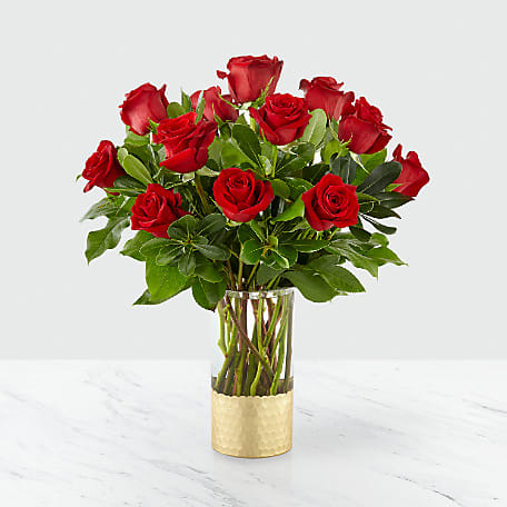 Red roses arranged in a clear glass vase with a gold wrap
