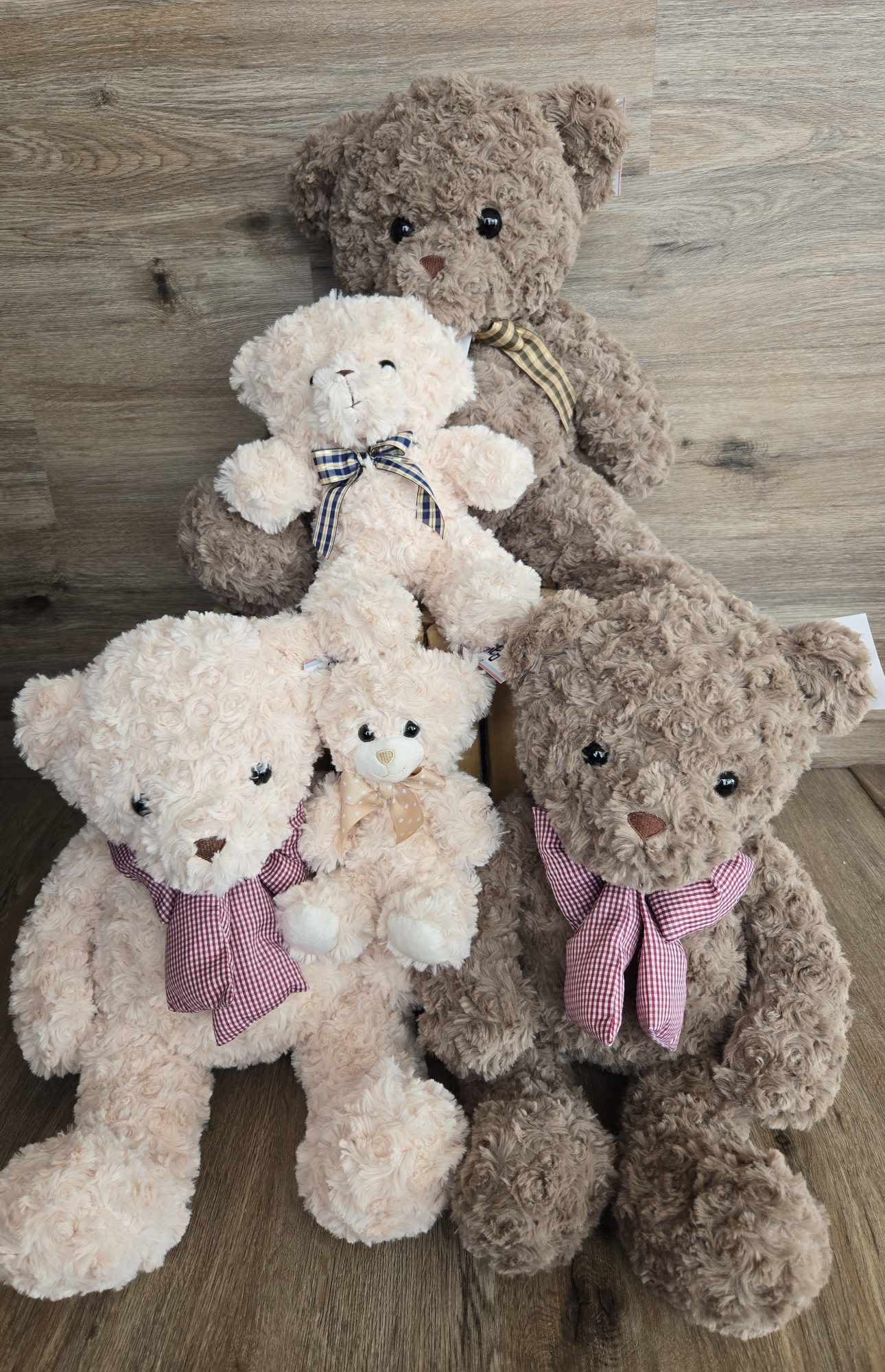 Four plush teddy bears with ribbon bows arranged on a wooden floor