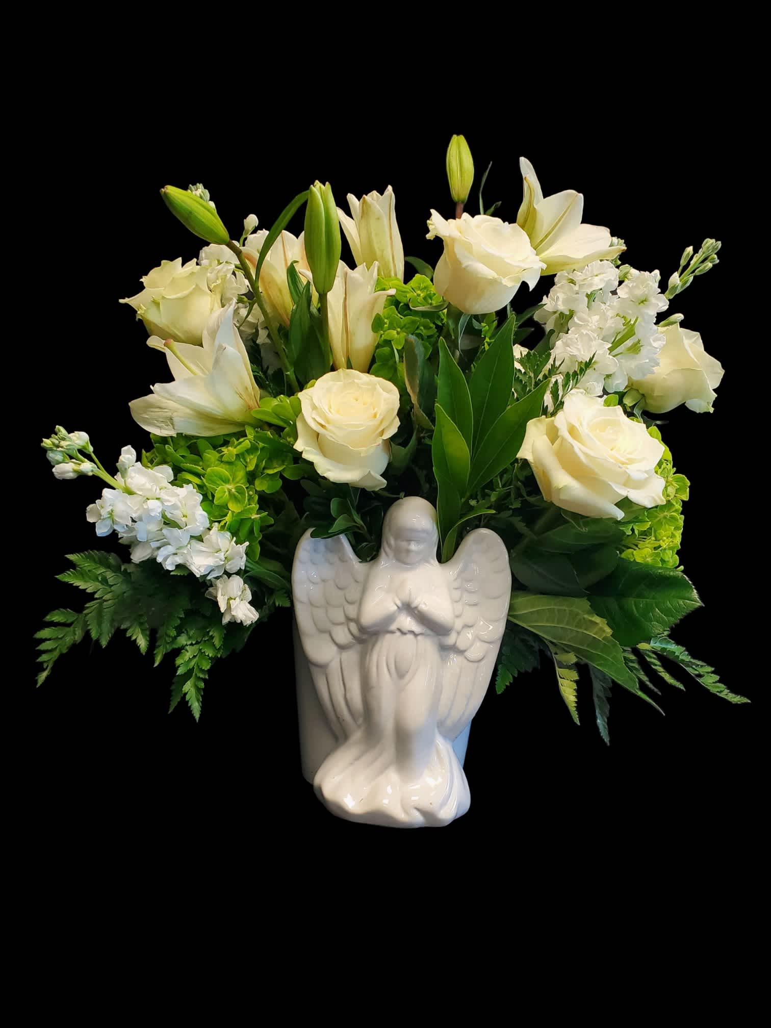 White roses and lilies arranged in a ceramic angel vase
