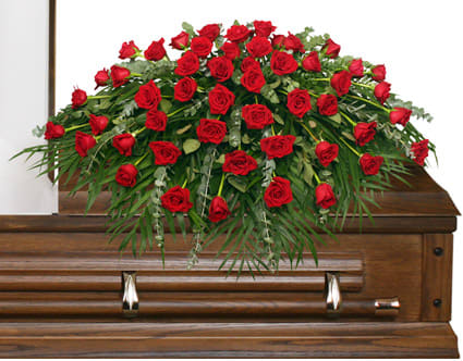 Red rose casket spray with greenery on a wooden casket