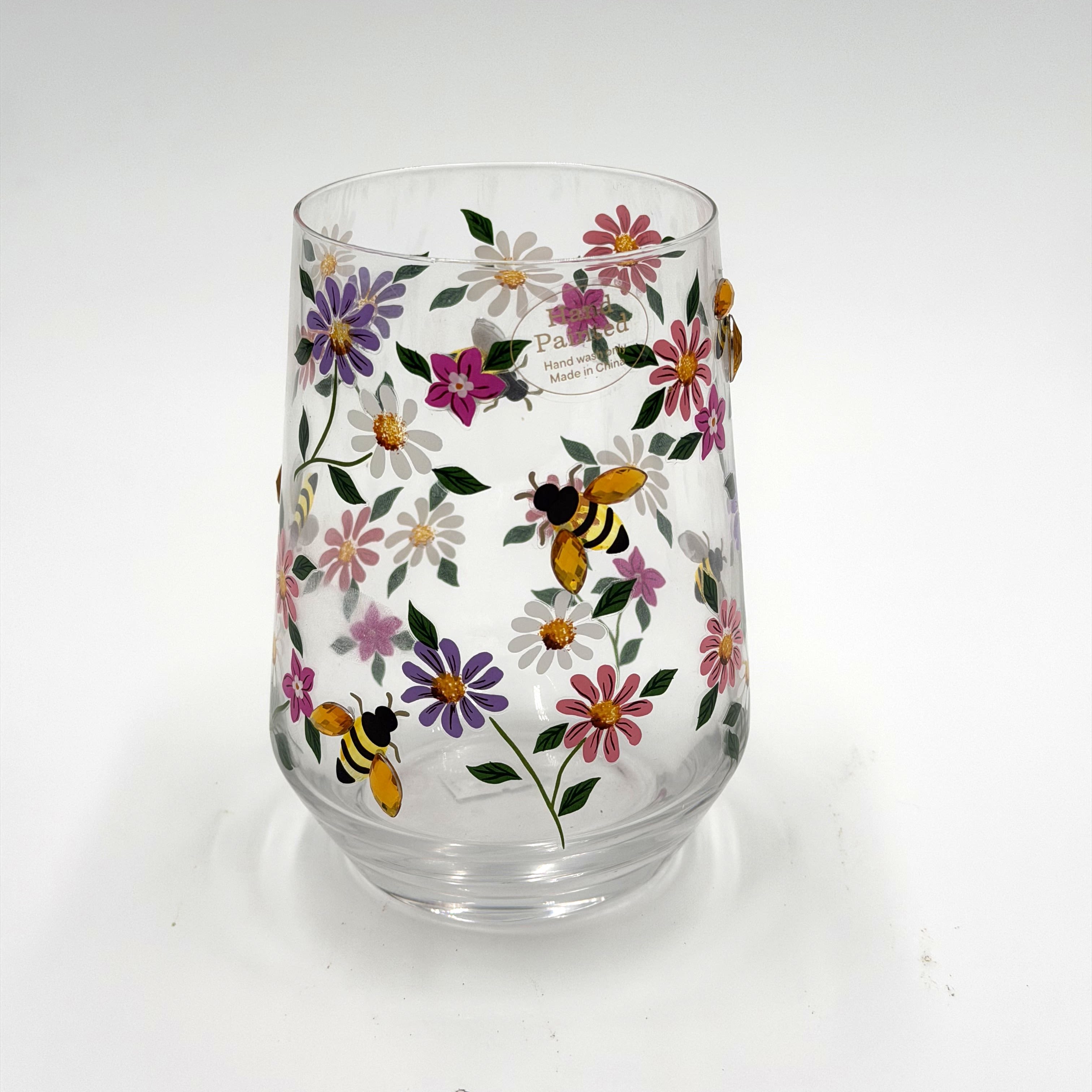 Hand Painted Tumbler - This charming hand-painted tumbler features a whimsical garden of colorful wildflowers accented with sparkling bee details for a cheerful, spring-inspired look. Delicate floral artwork wraps around the clear glass, creating a bright and playful design that feels both elegant and fun. Perfect for iced coffee, tea, cocktails, or everyday sipping, this tumbler adds a touch of sunshine to any occasion.