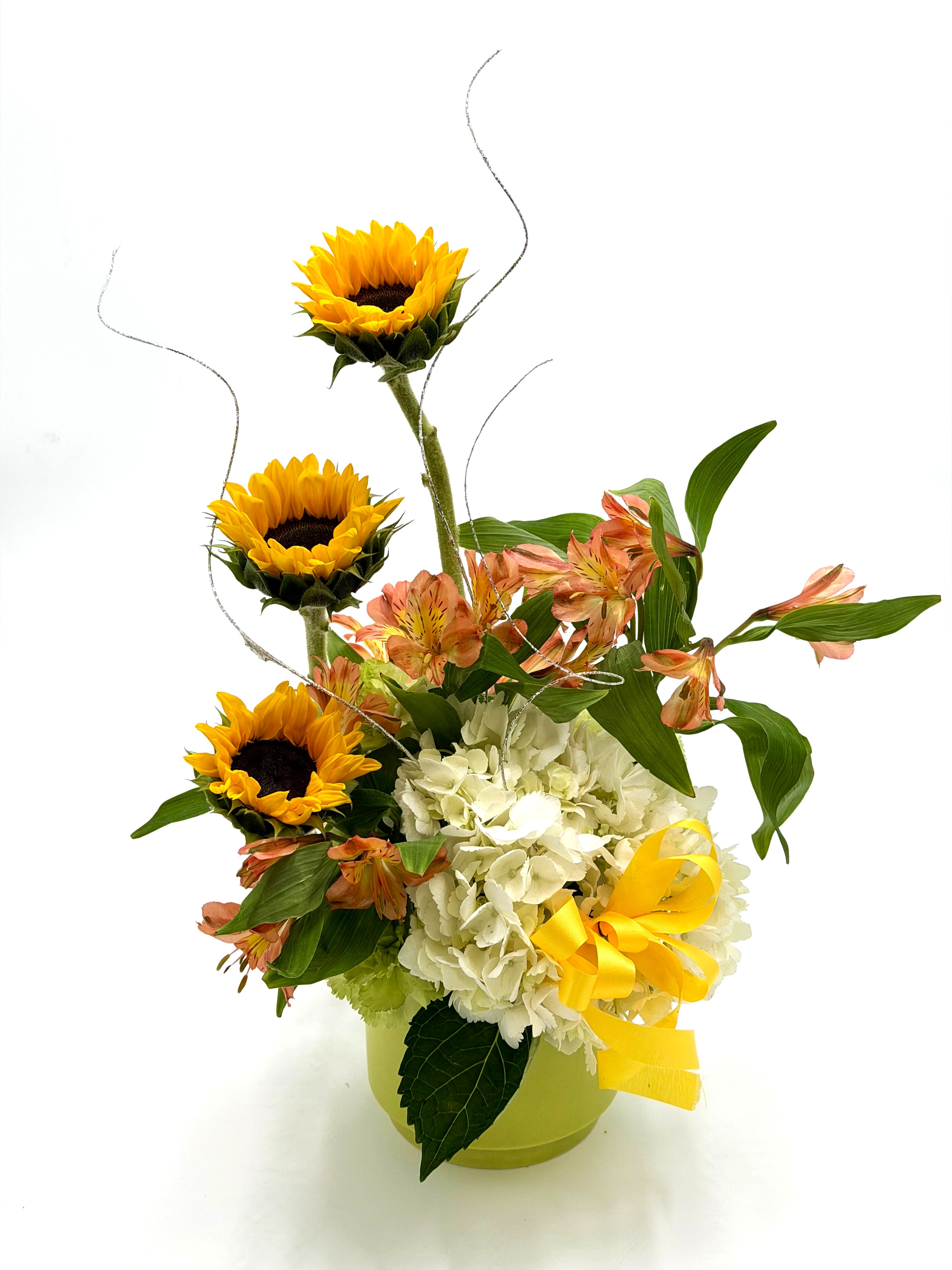 Sunshine and Grace - Sunshine and Grace is a cheerful arrangement that brings warmth and elegance together in one radiant design. Bright sunflowers rise above soft white hydrangea and delicate peach alstroemeria, creating a beautiful balance of bold color and gentle charm. Designed in a keepsake container with flowing accents and a sunny ribbon, this arrangement is perfect for celebrating life’s happiest moments.