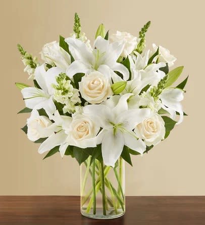 White lilies and cream roses arranged in a clear glass vase