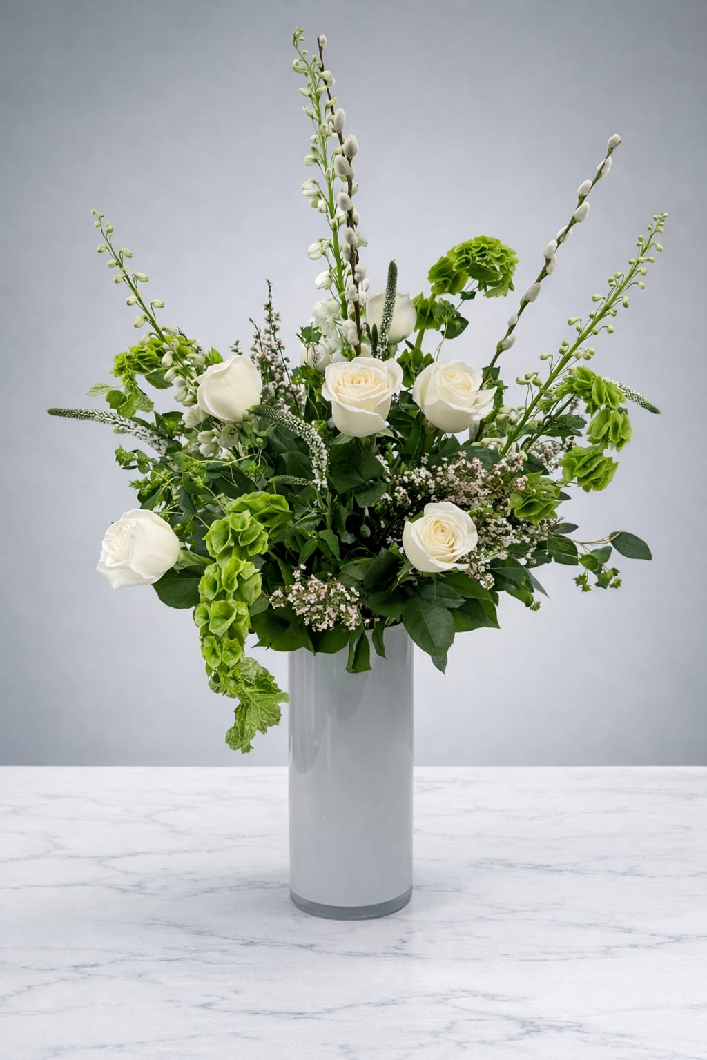 White roses and green blooms arranged in a tall glass vase