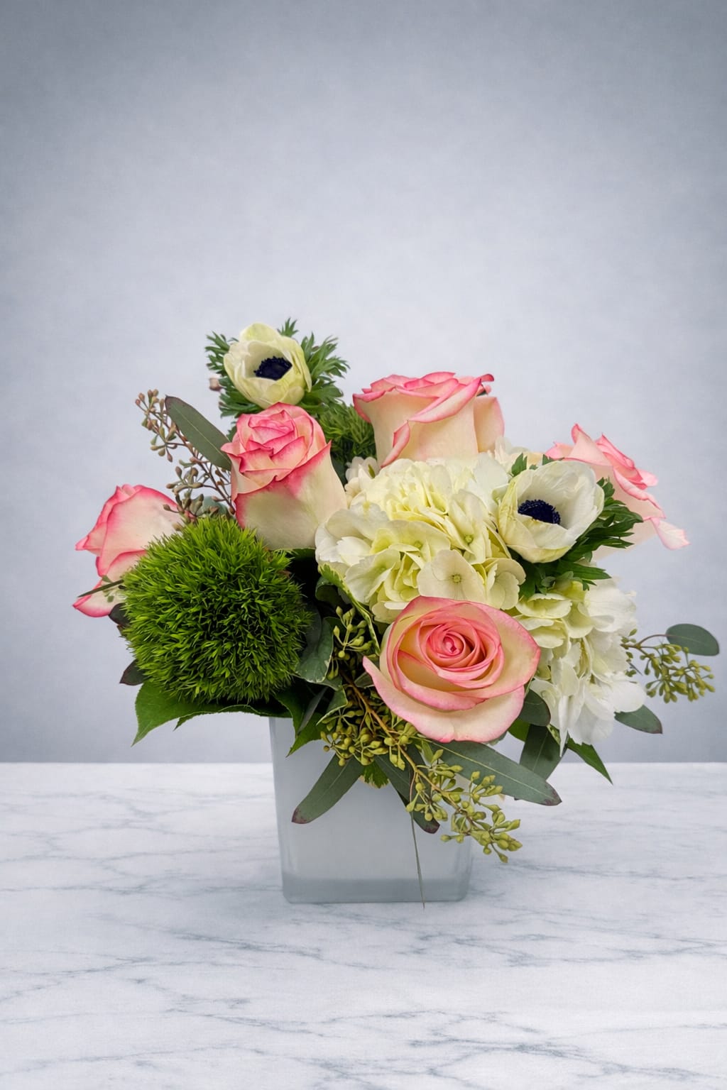 Pink-edged roses and white blooms in a square glass vase