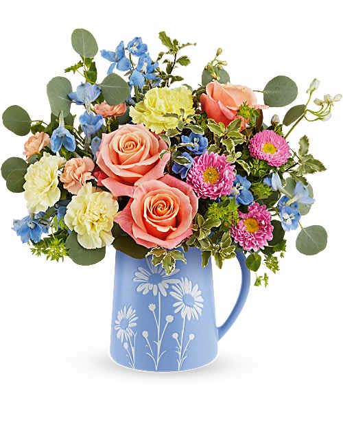 Mixed bouquet of roses, carnations, and daisies in a blue pitcher vase