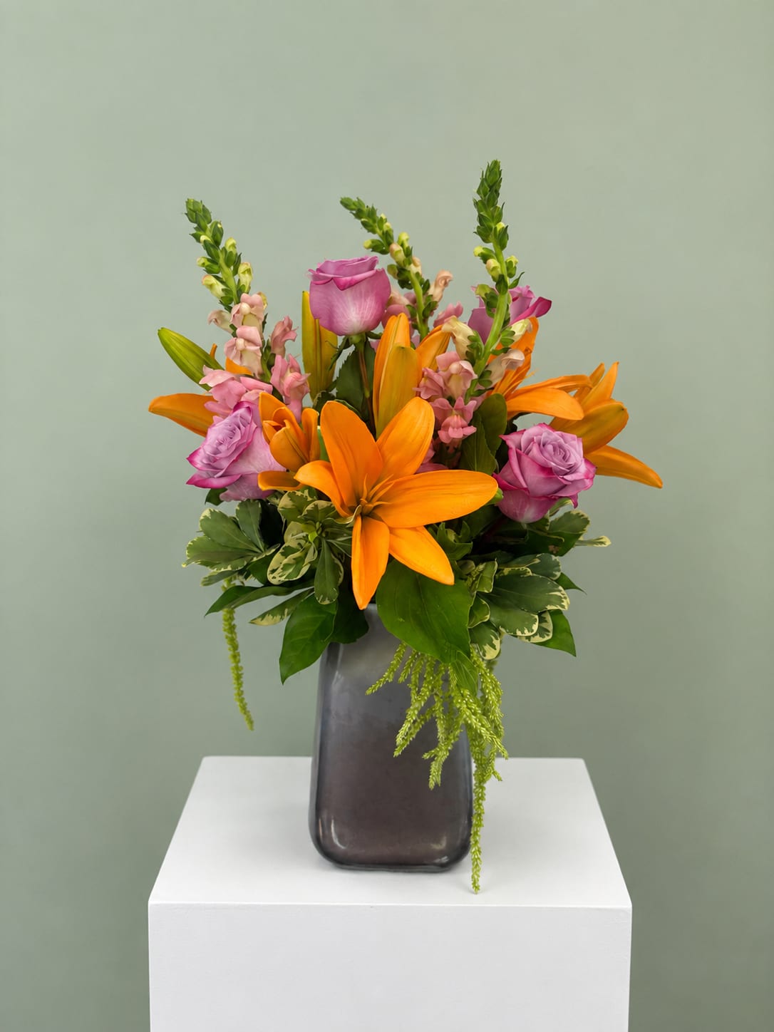 Orange lilies and pink roses in a dark vase