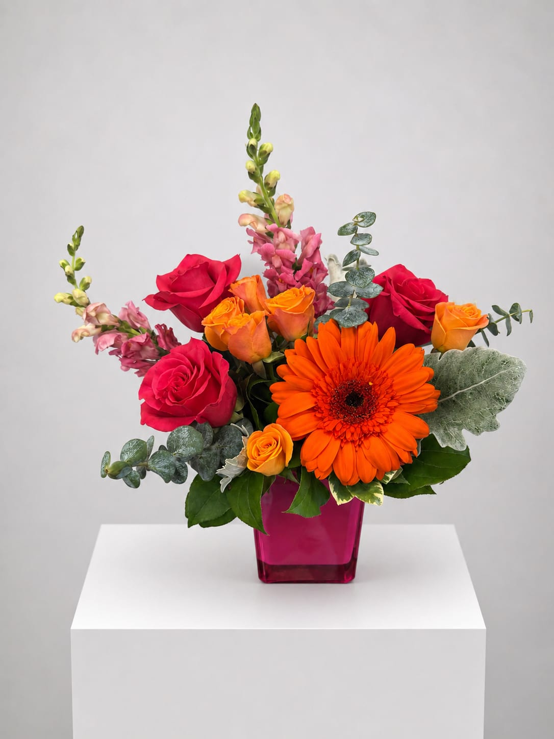 Bouquet of red and orange roses with a bright orange gerbera in a pink vase