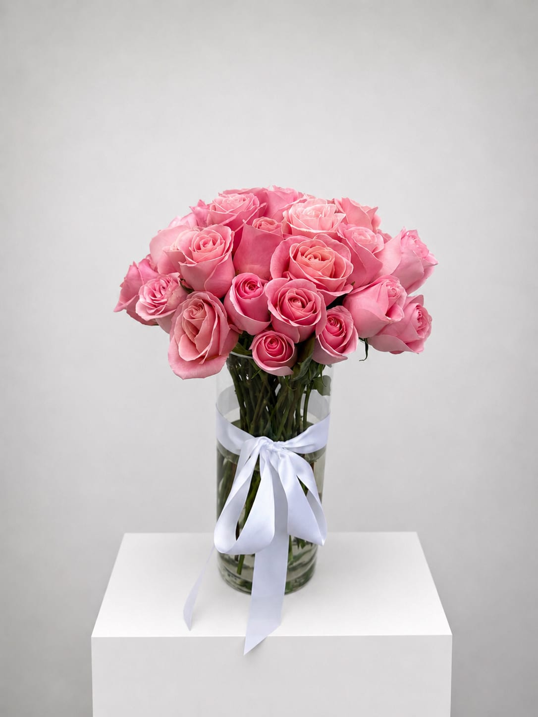 Pink roses arranged in a clear glass vase with a white ribbon