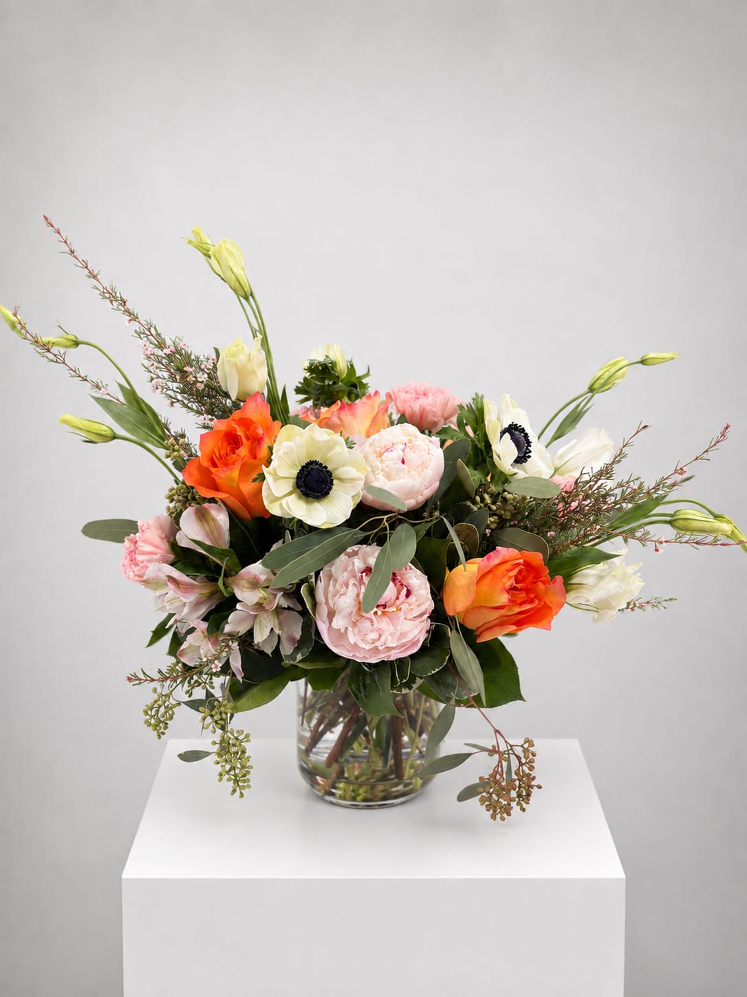 Mixed bouquet of orange, pink, and white flowers in a clear glass vase