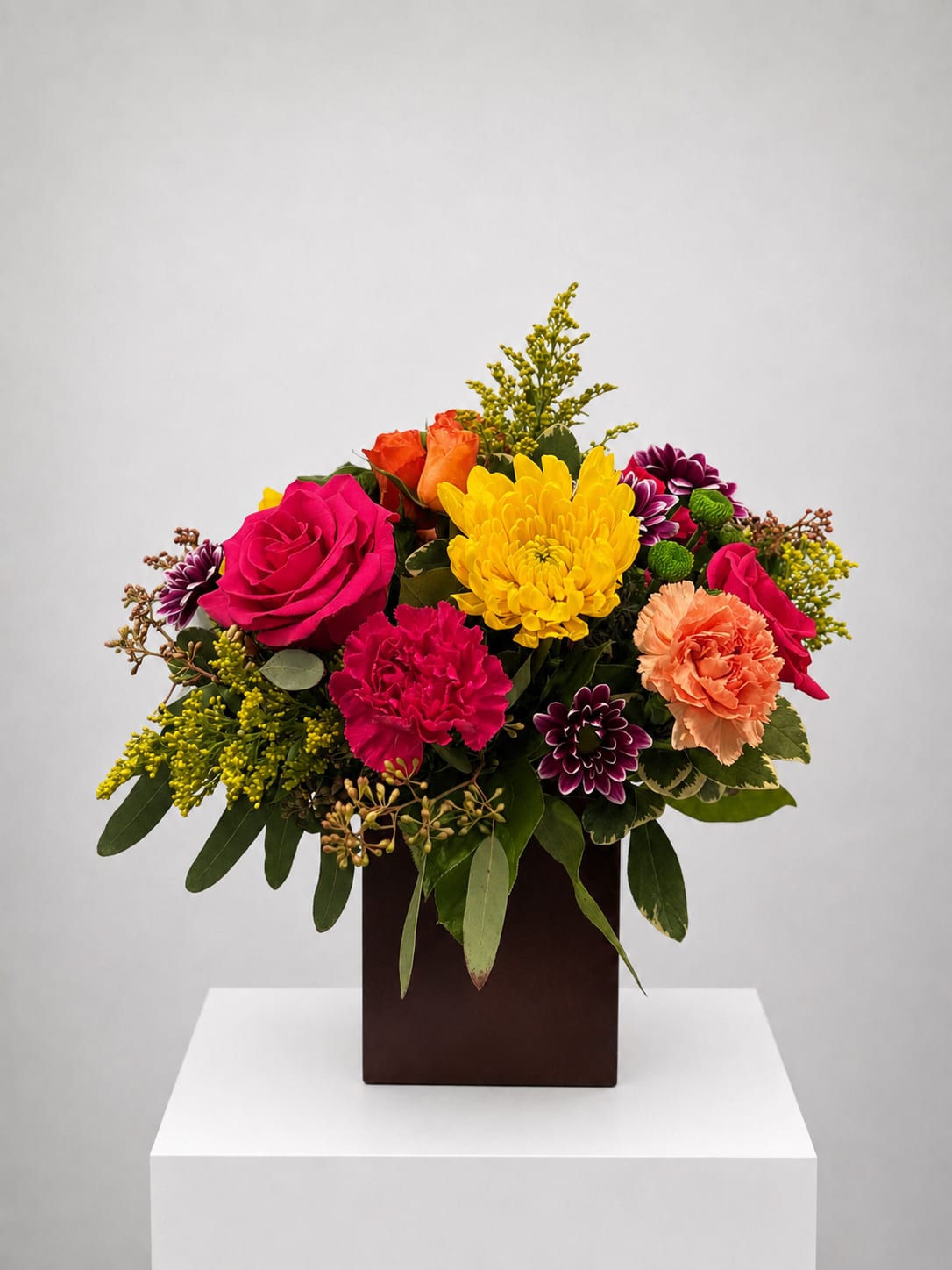 Colorful mixed bouquet in a dark square vase with roses, carnations, and chrysanthemums