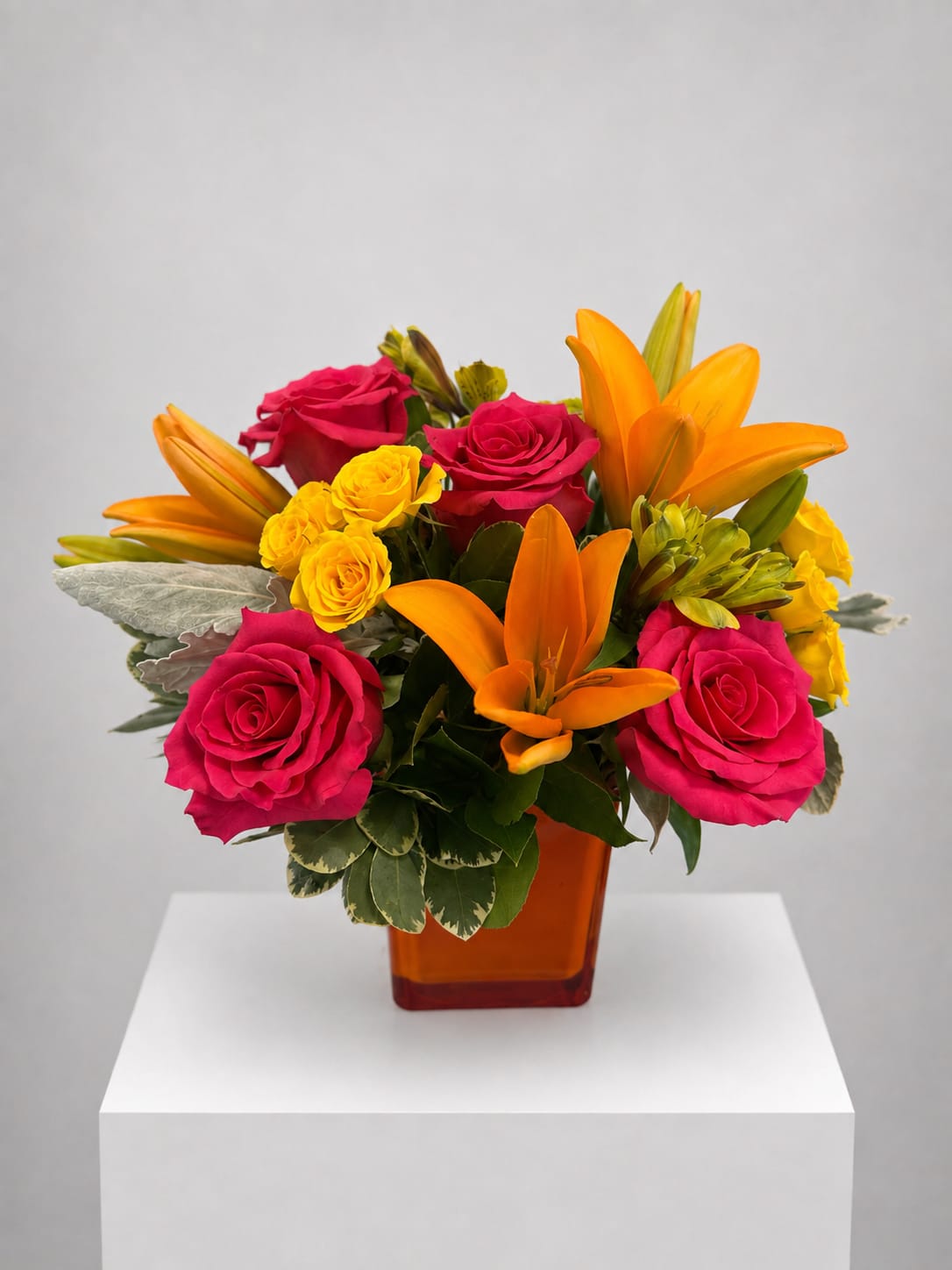 Bouquet of pink roses, yellow spray roses, and orange lilies in an amber vase