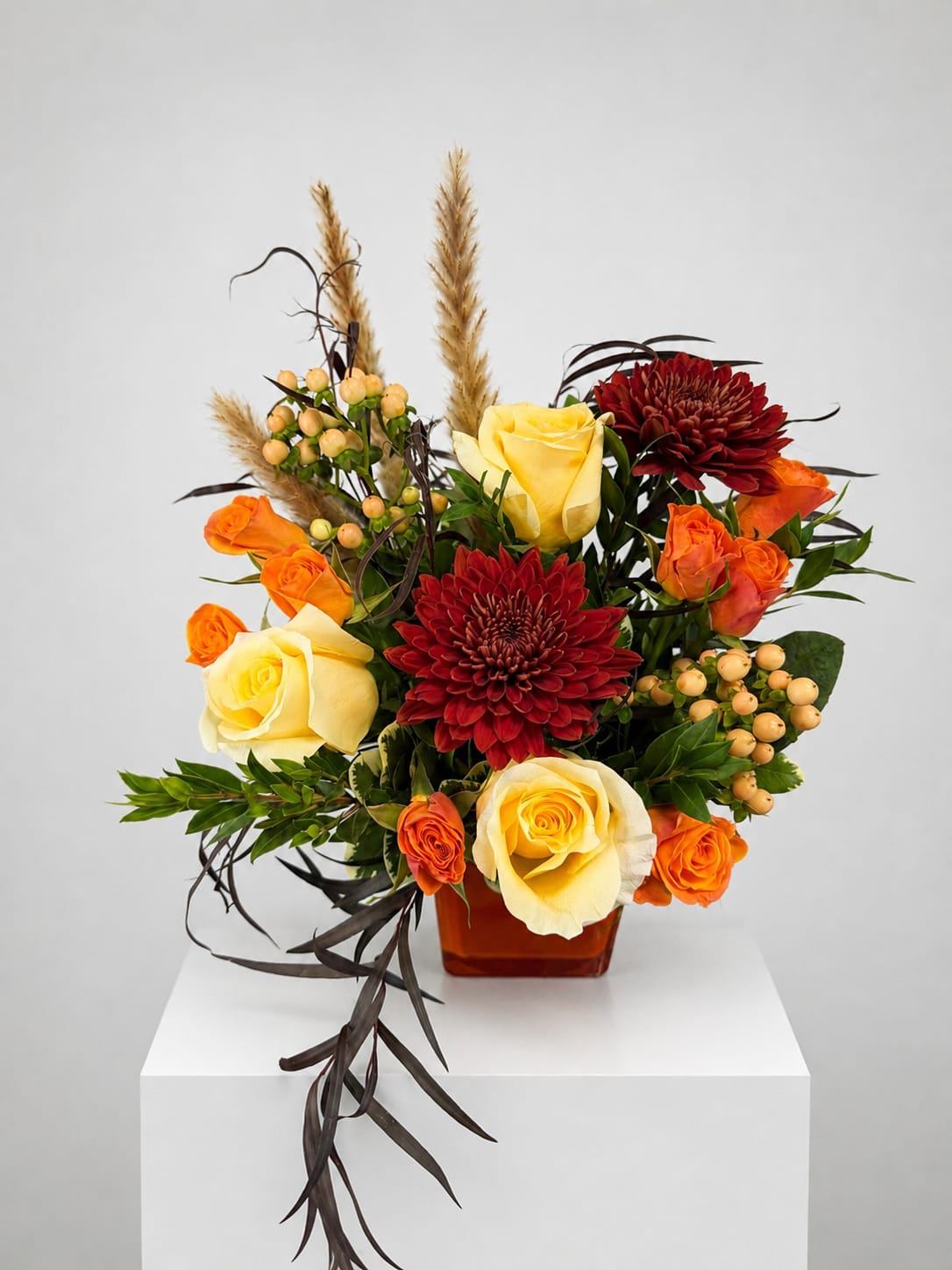 Arrangement of yellow and orange roses with red chrysanthemums in a square vase
