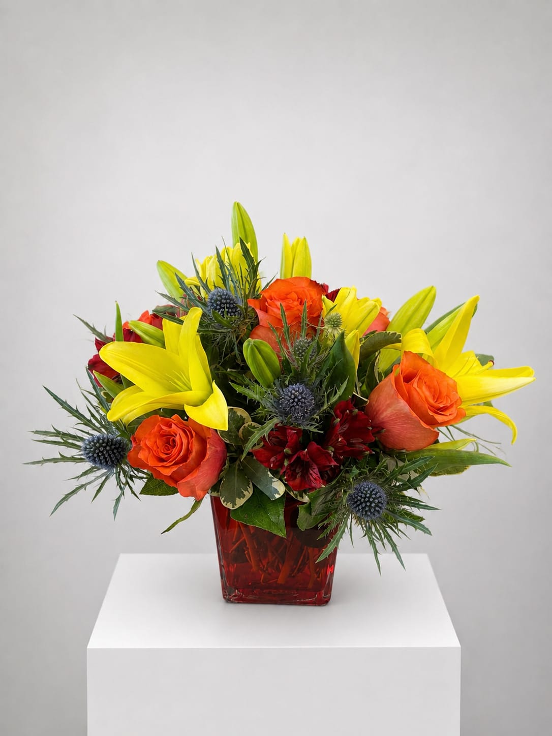 Orange roses and yellow lilies in a red glass vase