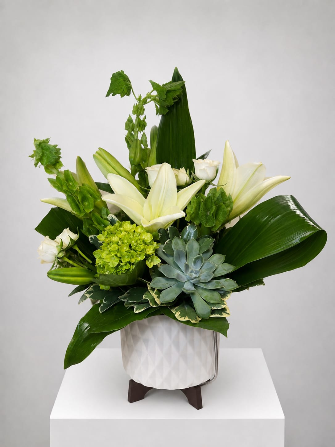 White lilies and green flowers in a white vase with a succulent accent