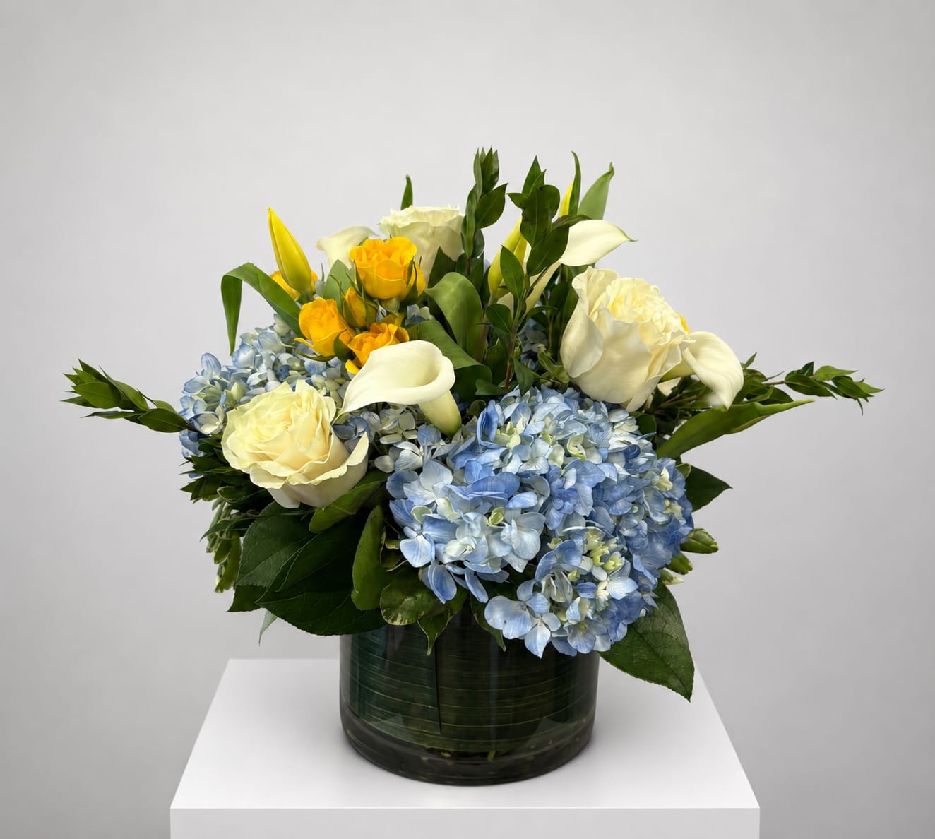 Blue hydrangeas with white roses and yellow calla lilies in a glass vase