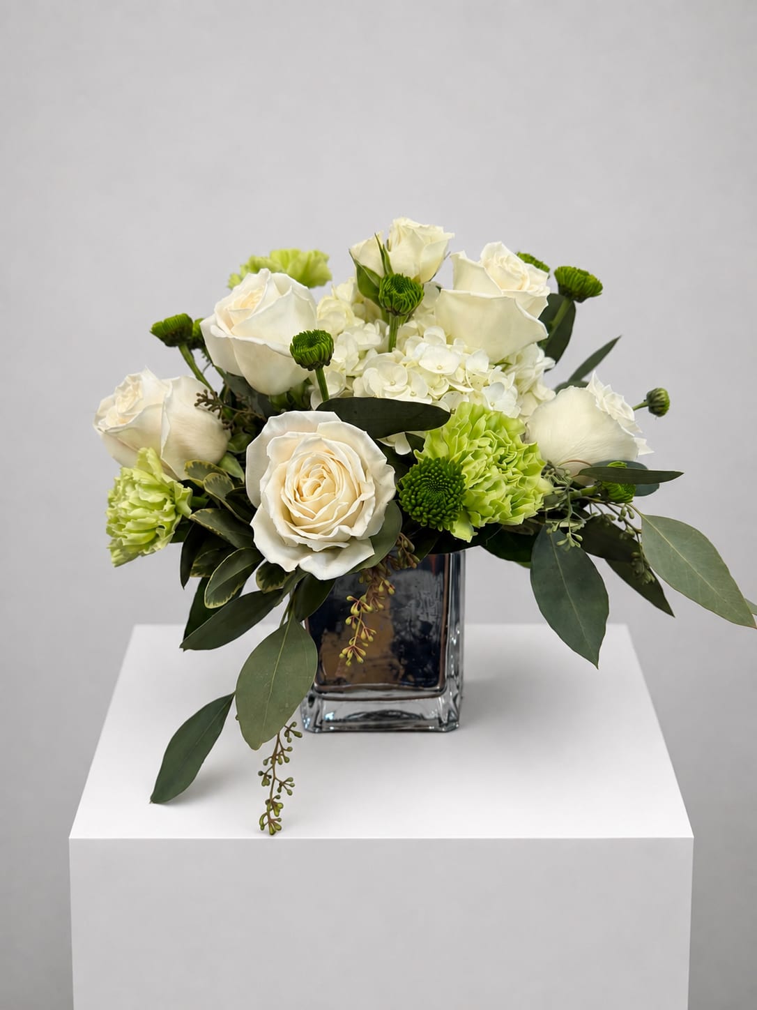 White roses and green carnations arranged in a clear square vase
