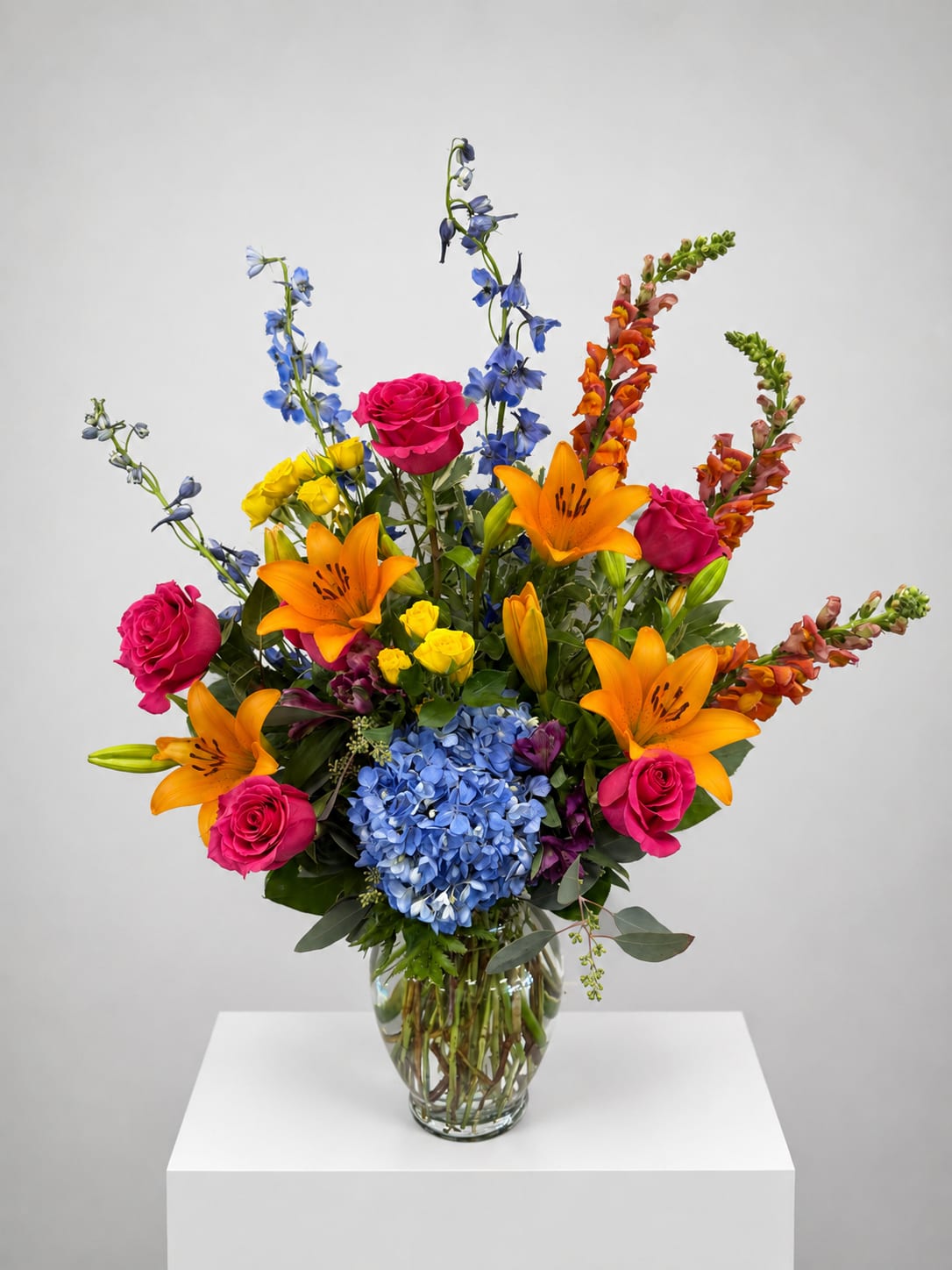 Bright mixed bouquet with roses, lilies, hydrangea, and blue delphinium in a glass vase