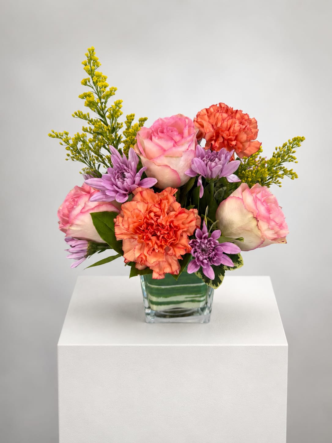 Pink roses, orange carnations, and purple daisies in a glass vase