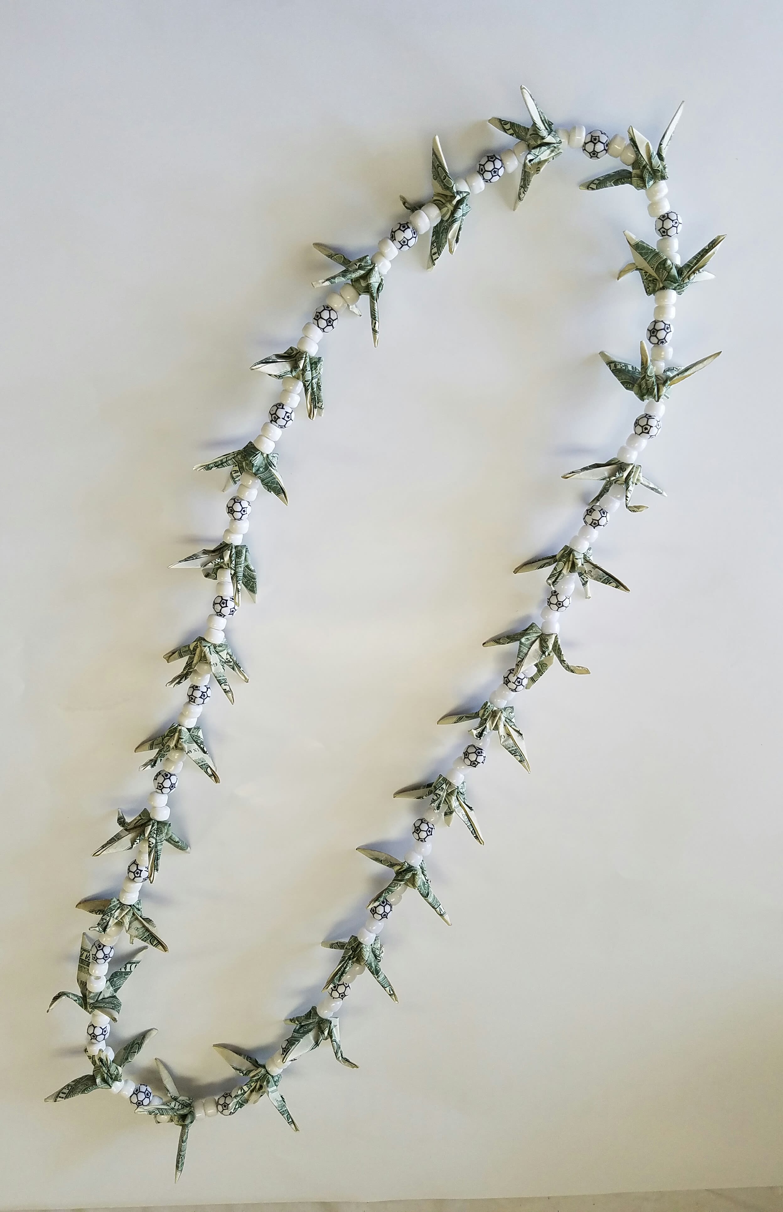 Beaded garland with folded dollar-bill shapes and white beads on a plain background
