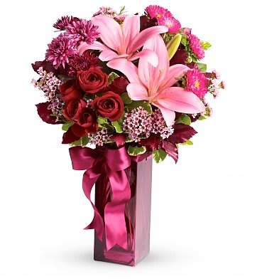 Bouquet of pink lilies and red roses in a tall pink vase with ribbon