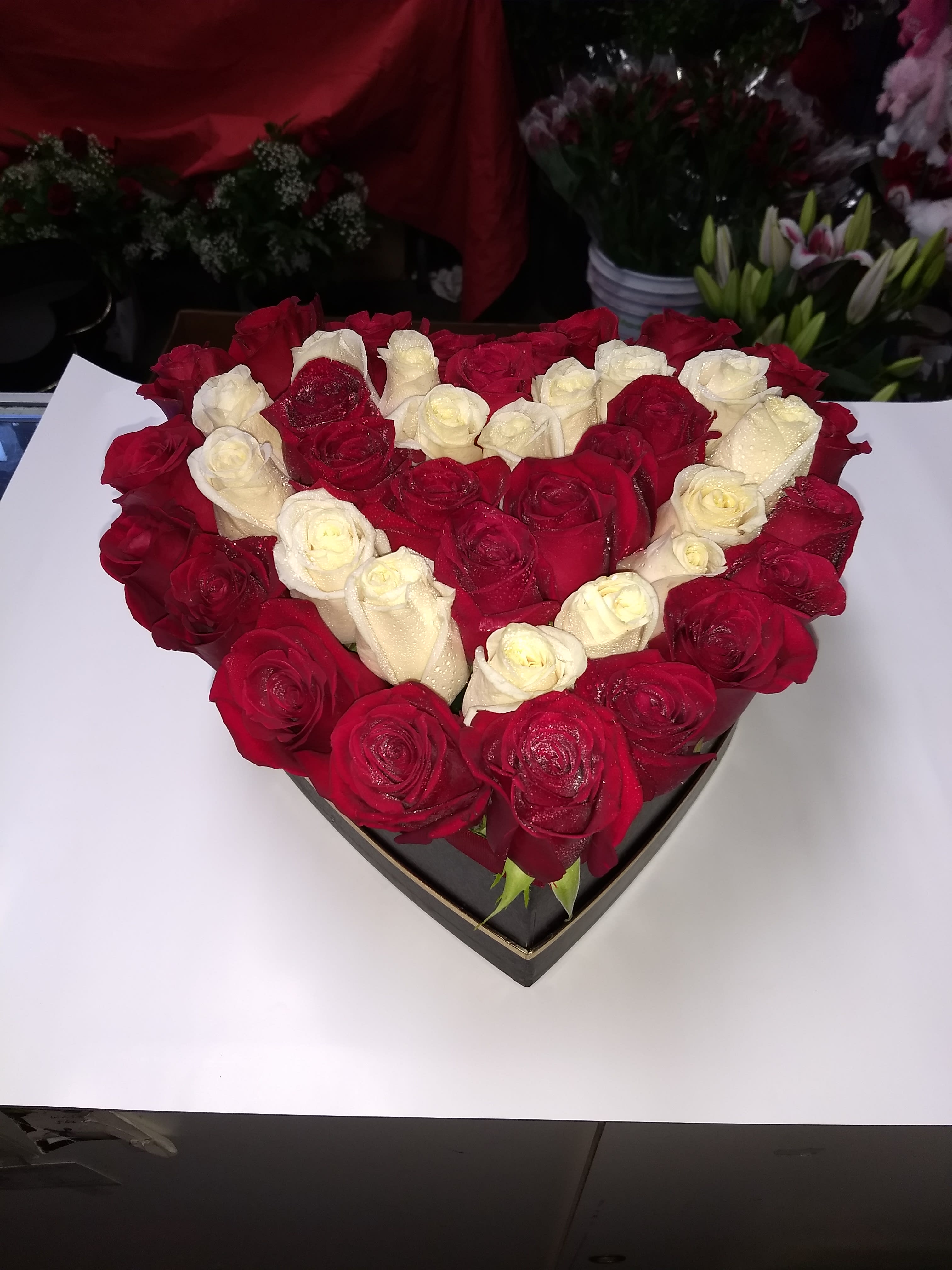 Heart-shaped arrangement of red and white roses in a black box