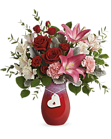 Red roses and pink lilies in a red vase with a heart charm