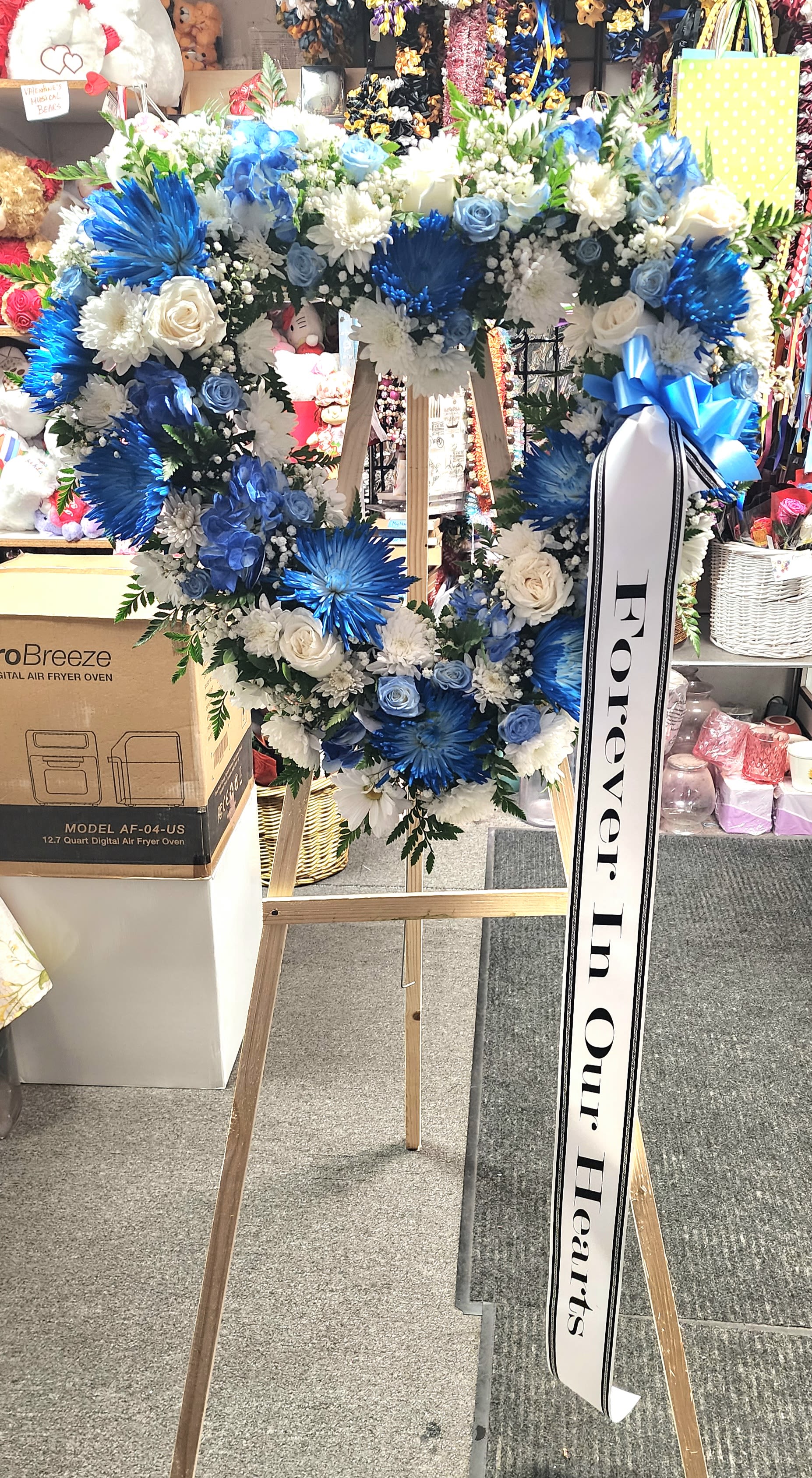 Blue and white floral heart wreath on a wooden easel with a memorial ribbon
