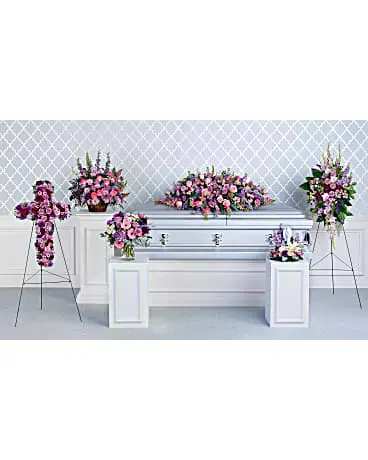 Pink and purple funeral floral arrangements around a silver casket