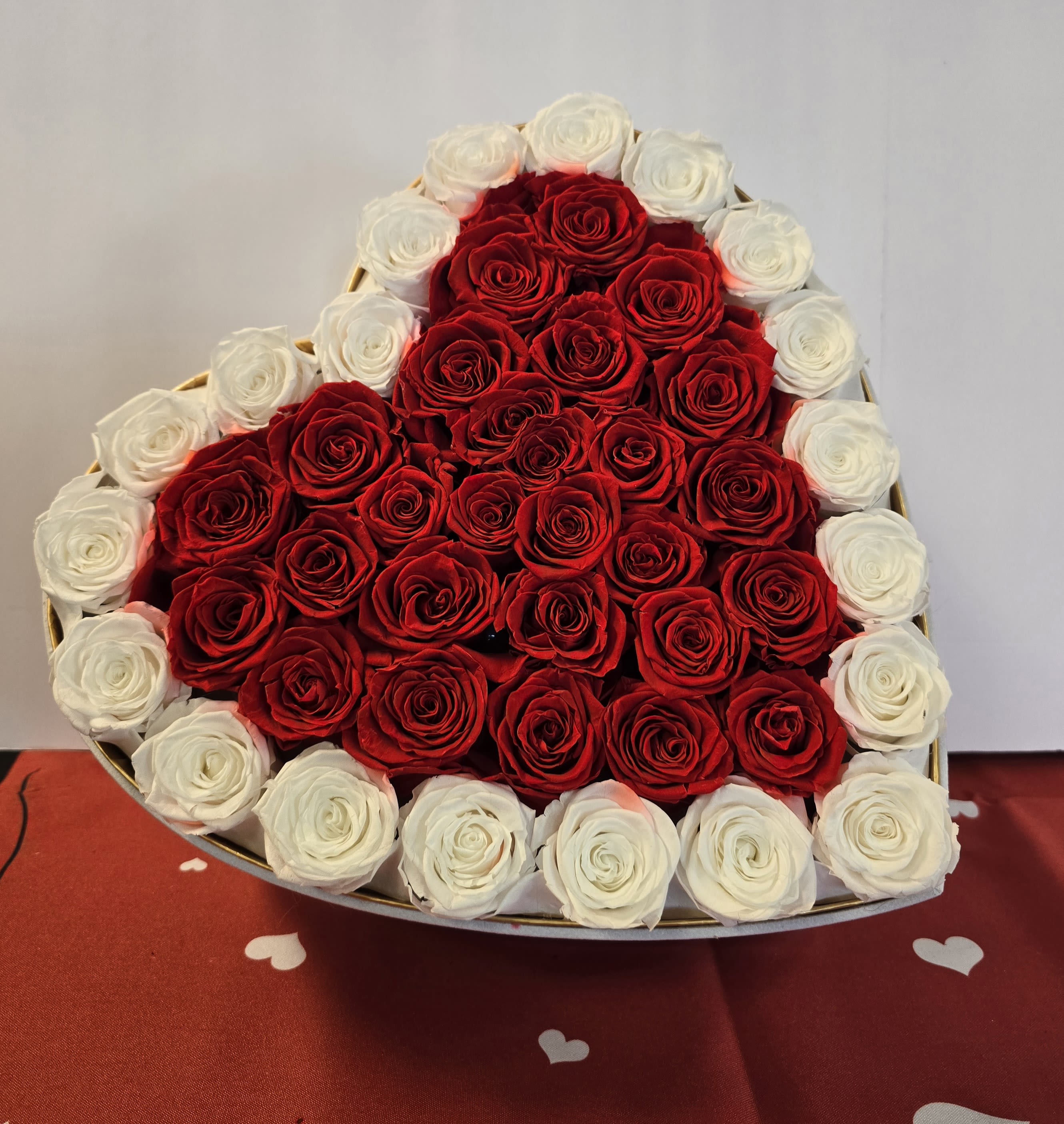 Heart-shaped box filled with red roses bordered by white roses.