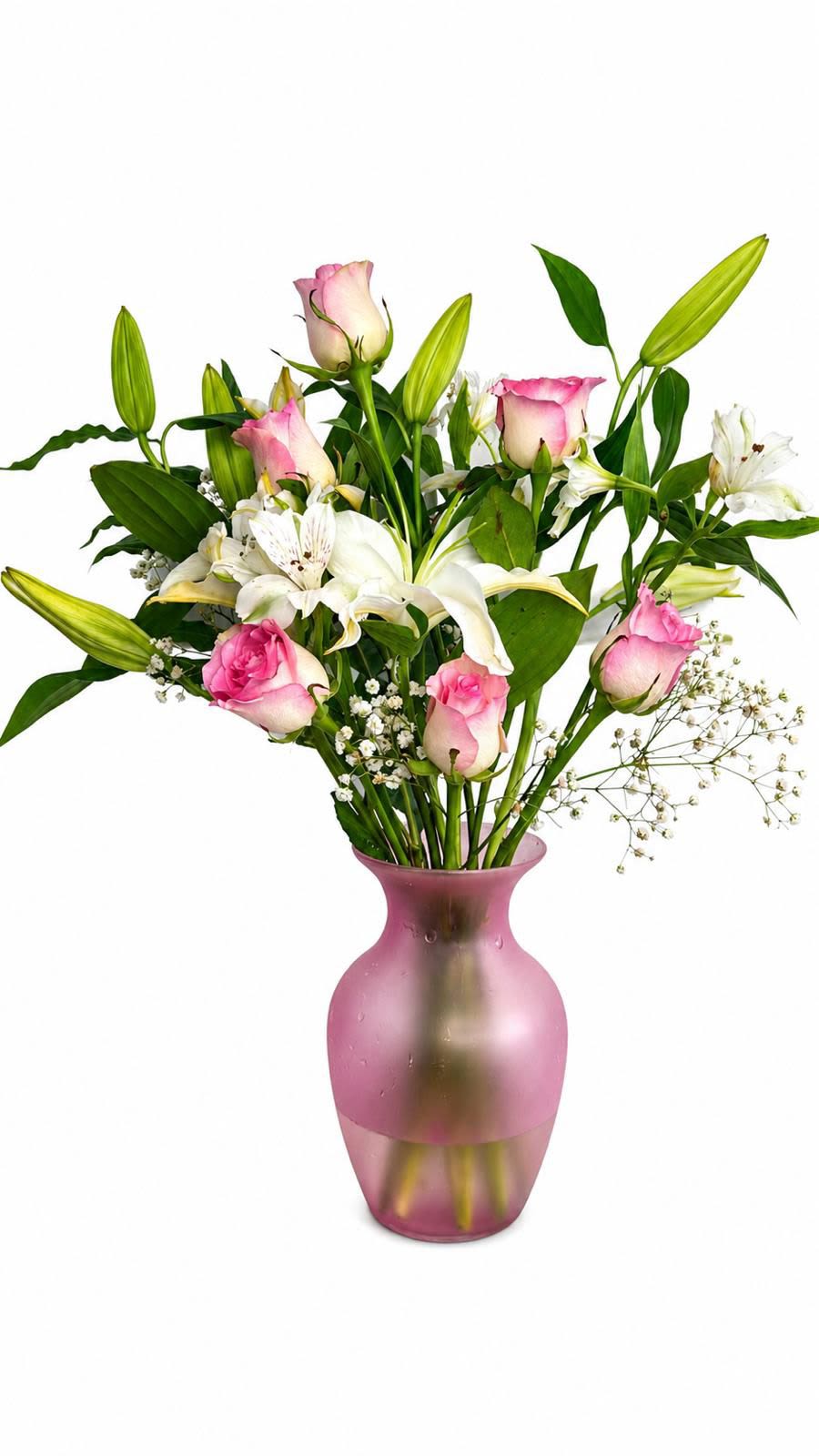 regalo de cariño - Soft pink roses and pure white lilies arrange themselves with airy white filler in a rounded pink glass vase to create a gentle, romantic flower arrangement perfect for a birthday bouquet, anniversary surprise, or a thoughtful sympathy arrangement. Regalo de cariño reads as quietly elegant and caring-the combination of soft pinks, bright whites, and fresh green accents makes the recipient feel comforted and cherished.  The design features loosely spaced blooms with several unopened lily buds for graceful height and a fresh, open silhouette that feels natural rather than formal. Textures contrast-velvety rose petals, sculpted lily blooms, and feathery filler-set in a blush-toned glass vase that adds a soft glow to tabletops or mantle displays. Sized for easy placement, it's a versatile everyday bouquet that communicates warmth and tenderness.  Whether you're celebrating an anniversary, marking a birthday, or sending a gentle message of sympathy, this arrangement offers a sincere way to show you care. Care is simple: keep water fresh and trim stems every few days to extend vase life, and place away from direct heat for the longest-lasting blooms.