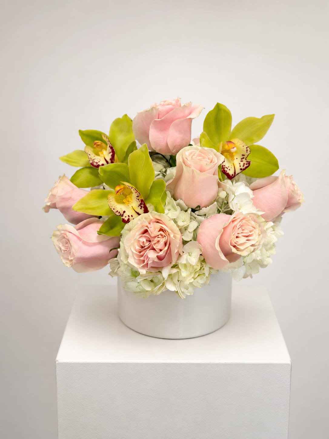 Pink roses and green orchids arranged in a white box vase