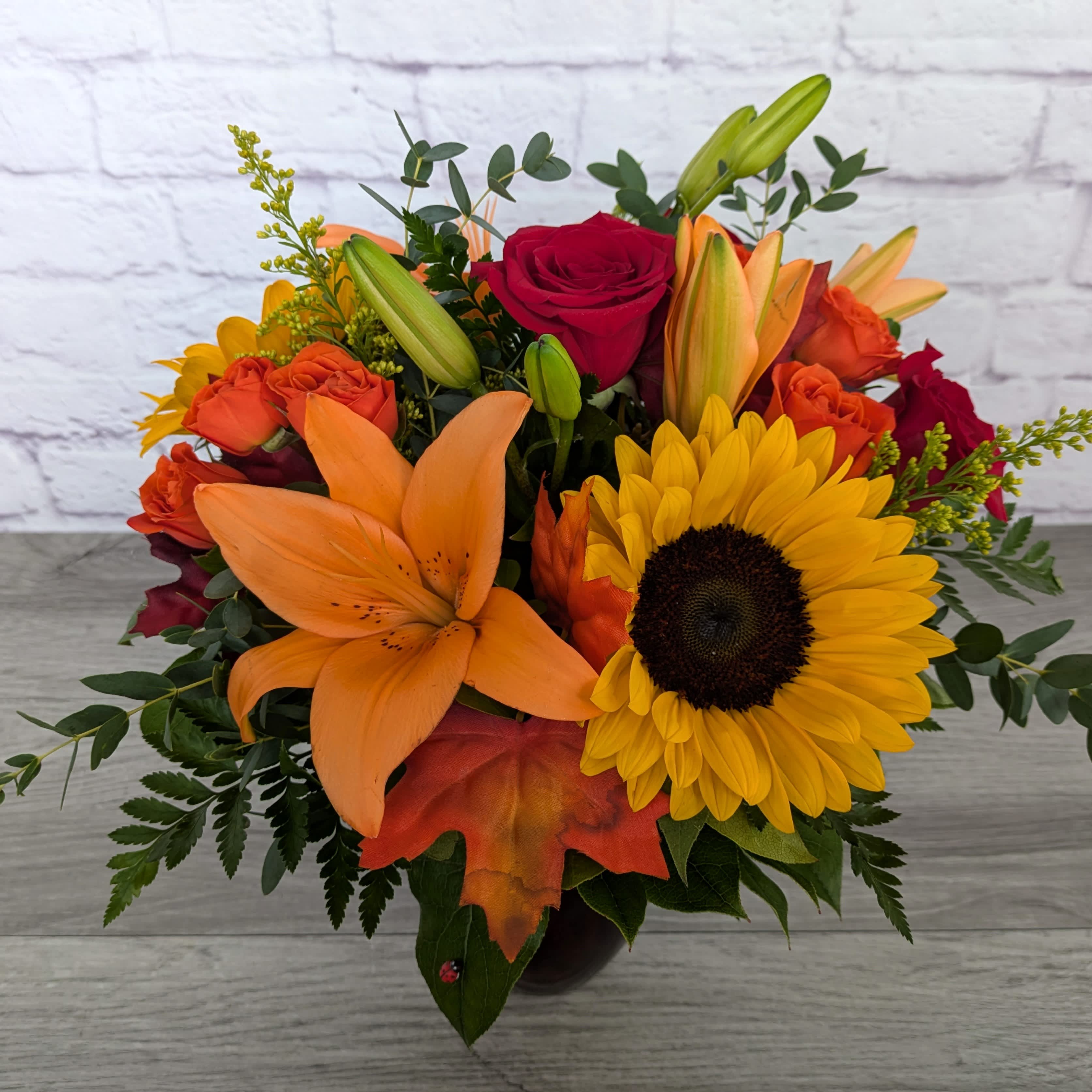 Bouquet of orange lilies, red roses, and a yellow sunflower in a vase