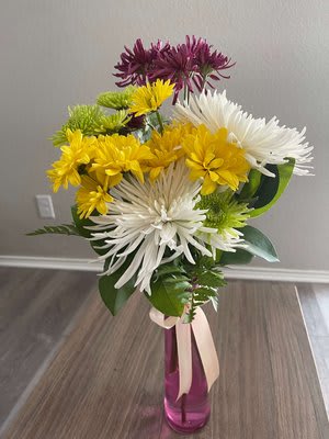 Bouquet of white, yellow, green, and purple chrysanthemum blooms in a pink vase