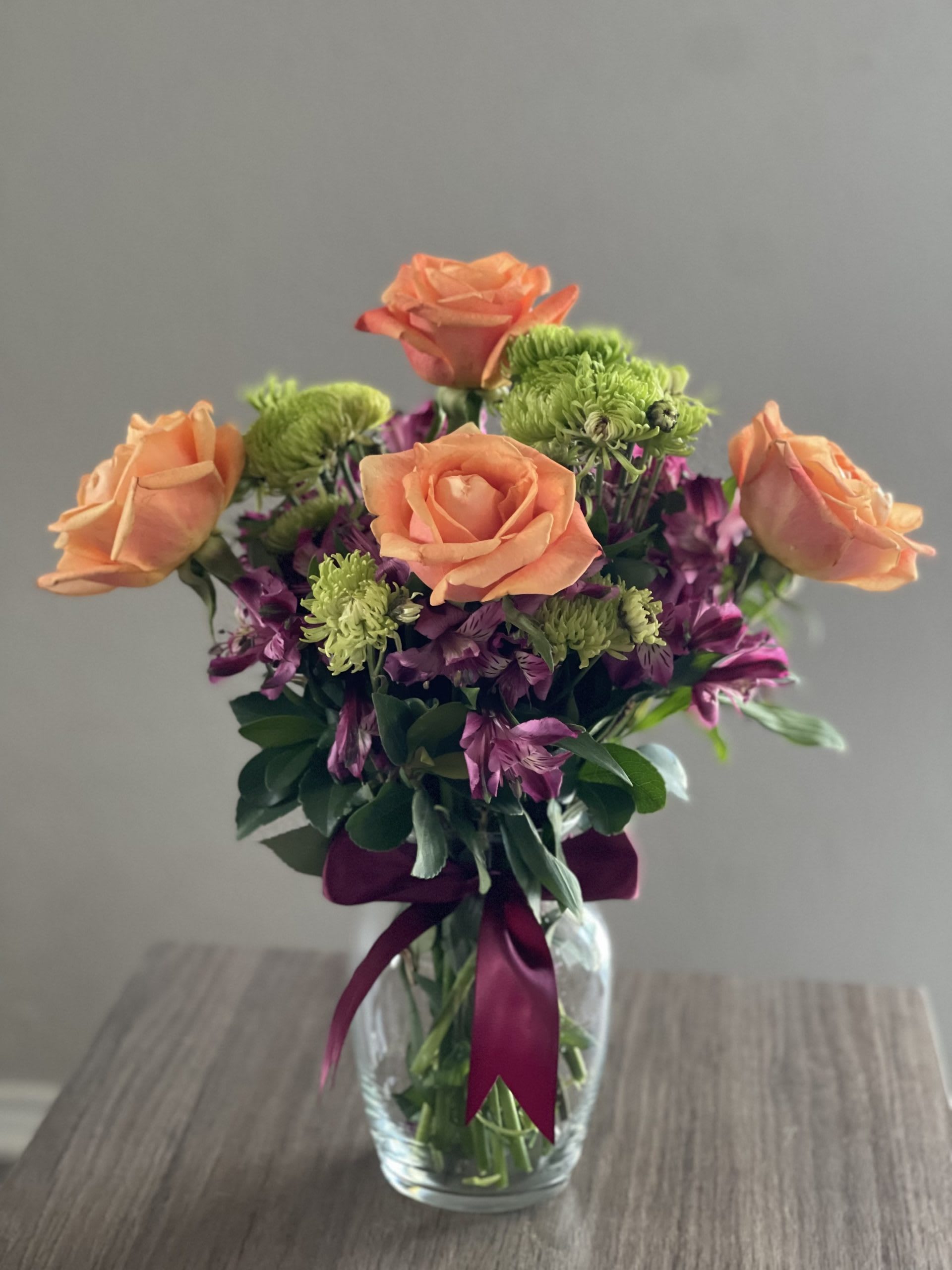 Peach roses and purple flowers in a glass vase with a ribbon