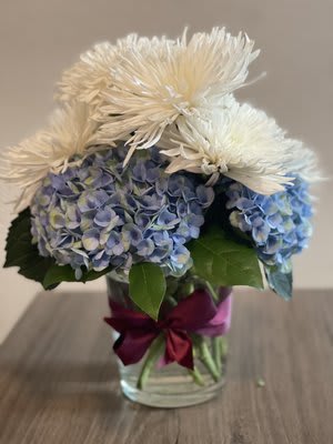 Blue hydrangeas and white spider mums in a glass vase with a ribbon