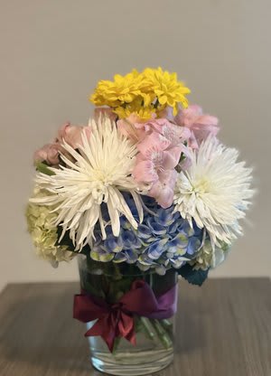 Mixed bouquet in a glass vase with white, pink, yellow, and blue flowers