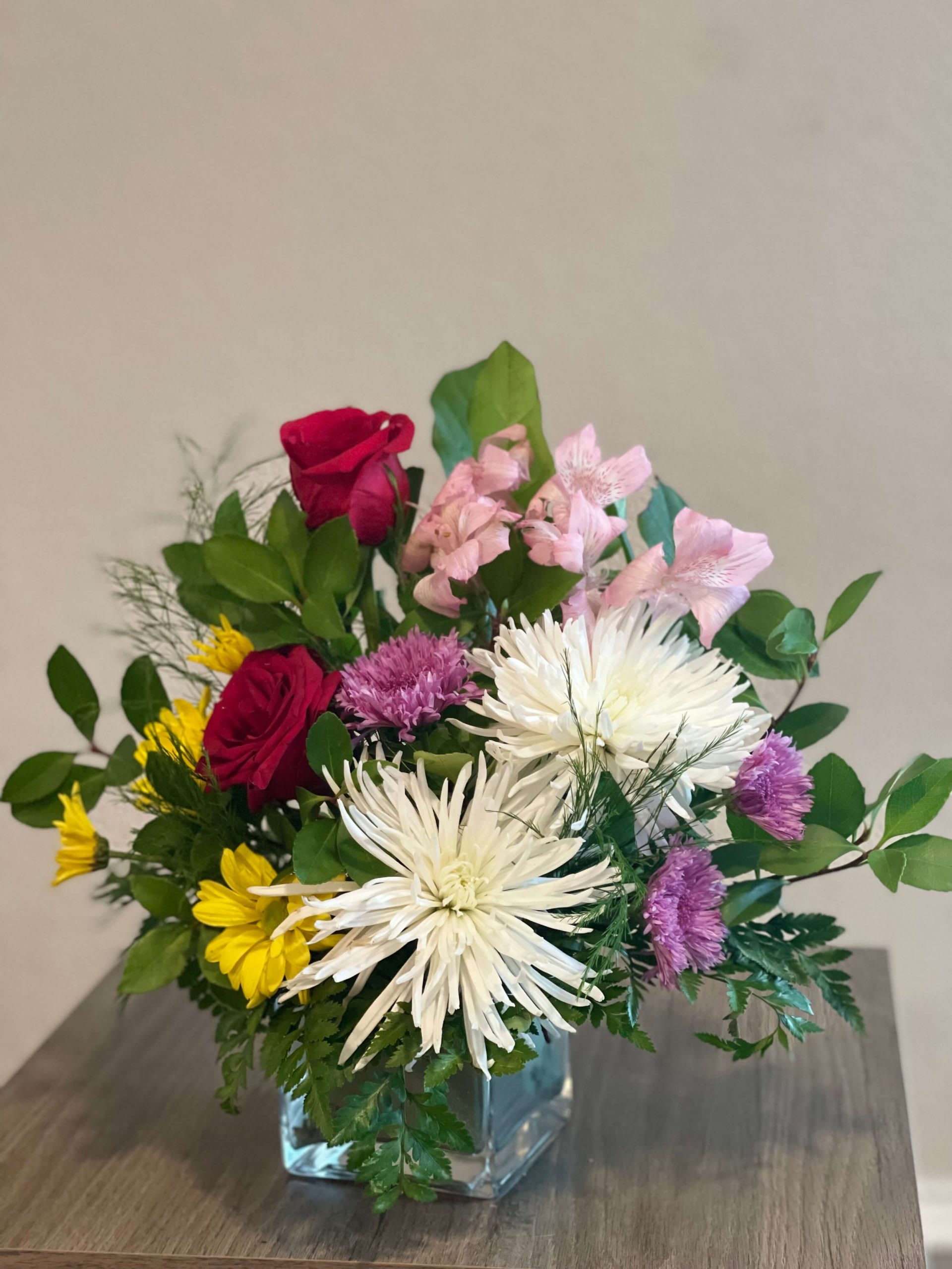 Mixed bouquet in a clear glass vase with red roses, white spider mums, and pink flowers