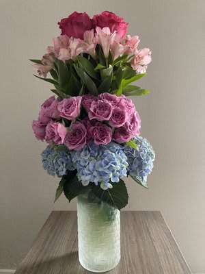 Tall bouquet of pink roses, alstroemeria, and blue hydrangeas in a glass vase
